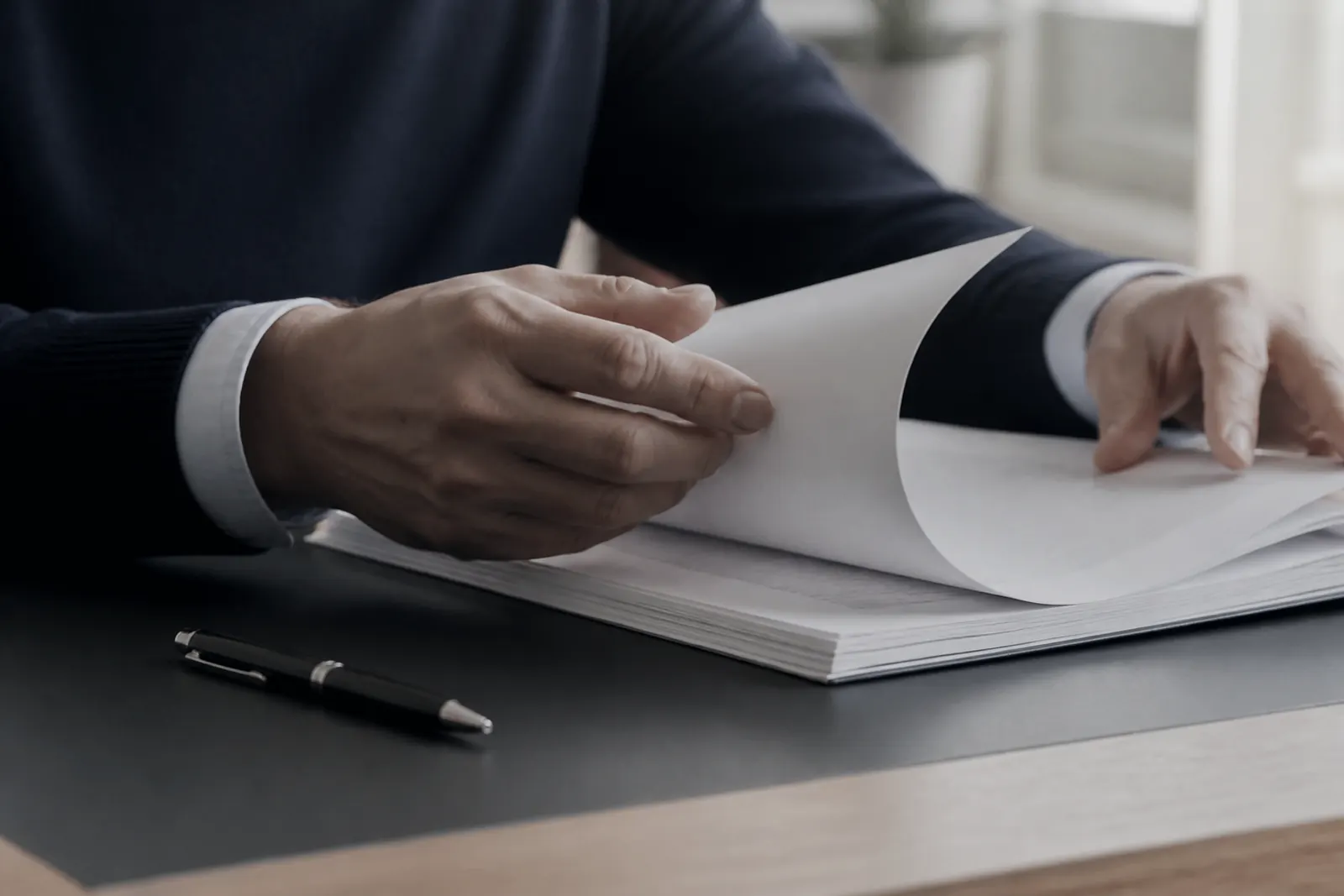 Mains feuilletant un contrat papier sur un bureau.