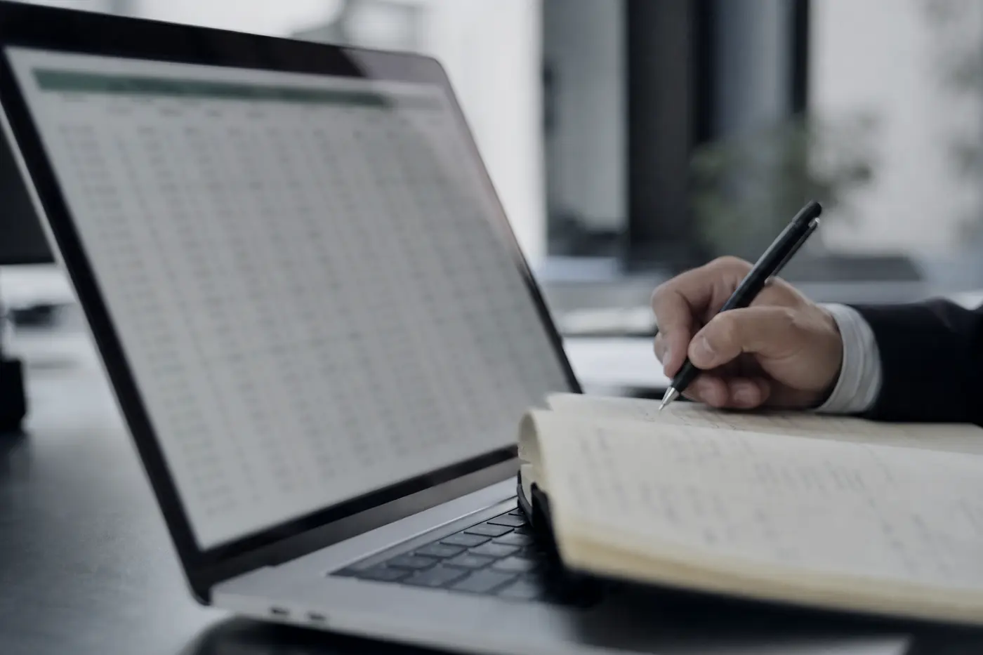 Plan serré sur un tableur affiché et une main annotant un carnet.