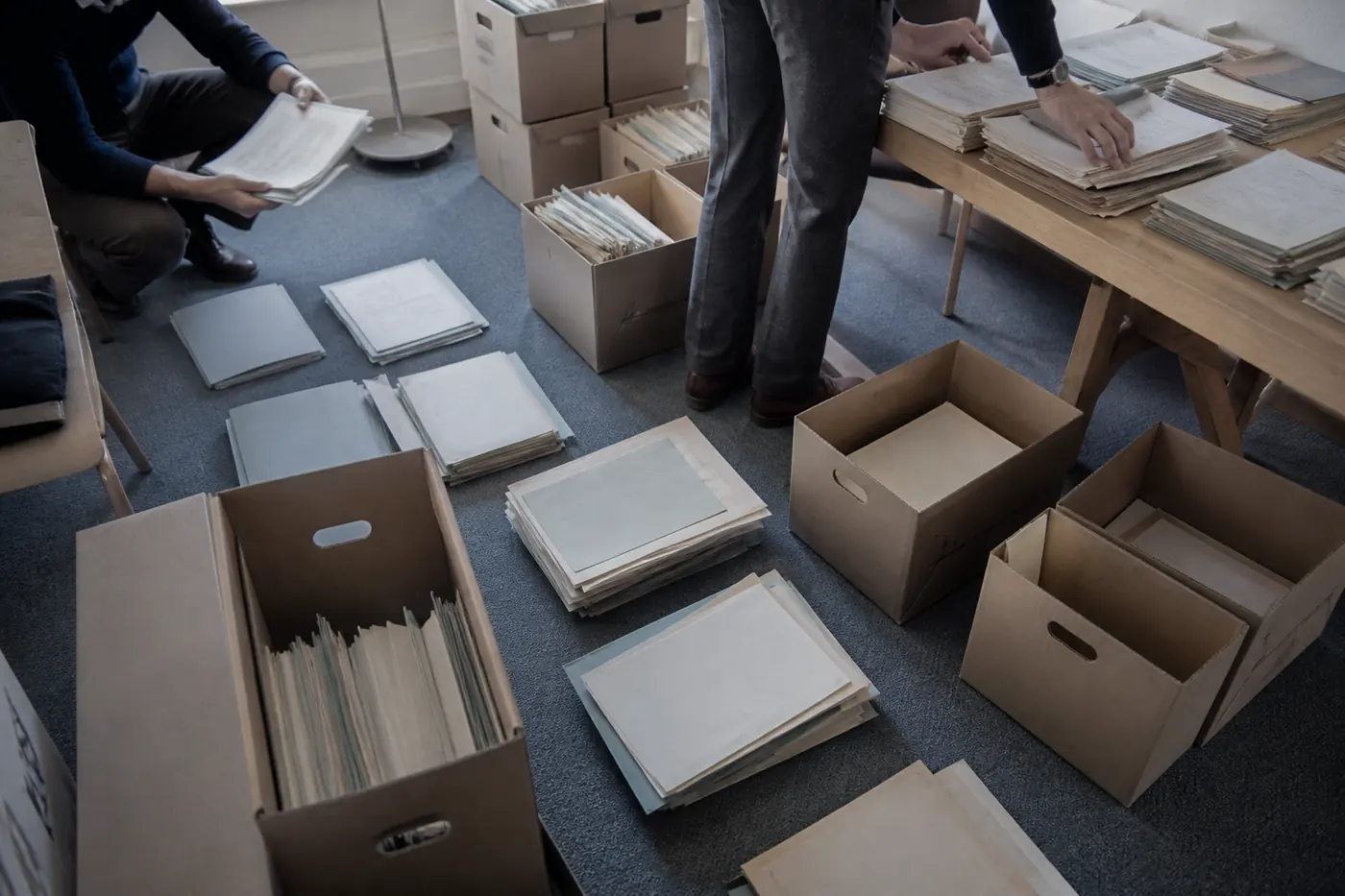 Boîtes d’archives ouvertes et documents étalés sur une table.