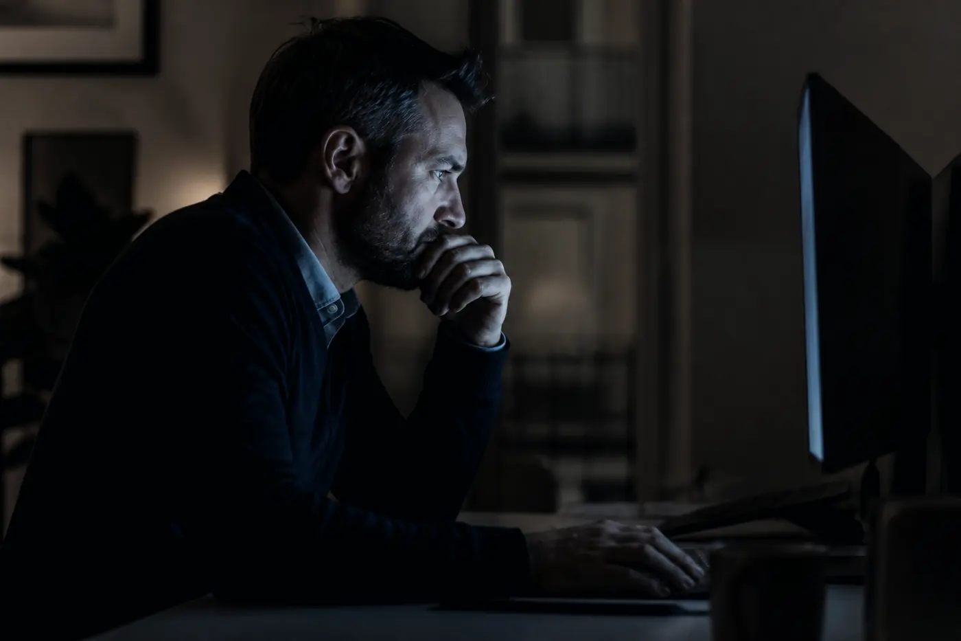 Personne concentrée devant un écran dans une pièce sombre.